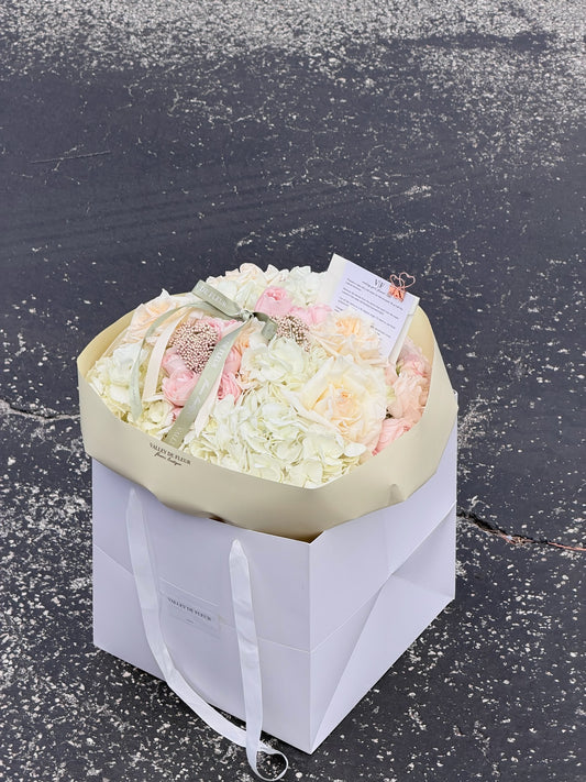 Soft hydrangeas and mixed roses wrapped as a blush birthday bouquet