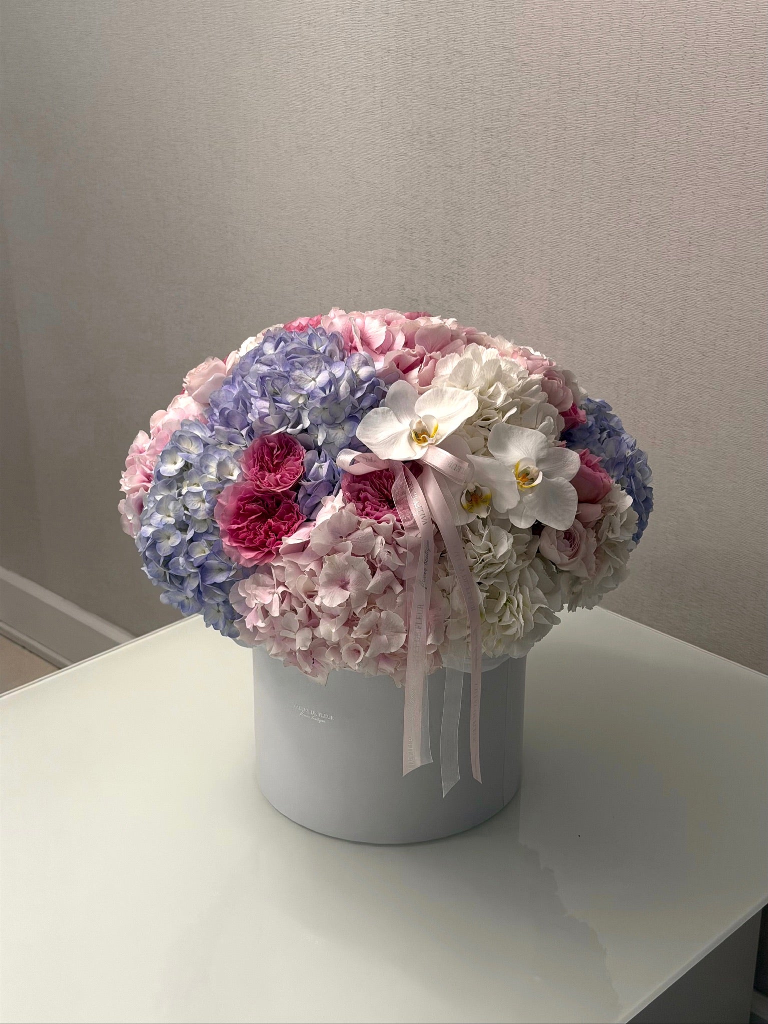 Pastel hydrangeas, garden roses and white orchids in a medium birthday flower arrangement
