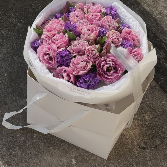 Light pink tulips with purple floral accents arranged in a lush romantic bouquet for an anniversary celebration