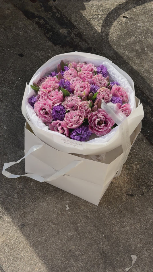 Light pink tulips with purple floral accents arranged in a lush romantic bouquet for an anniversary celebration
