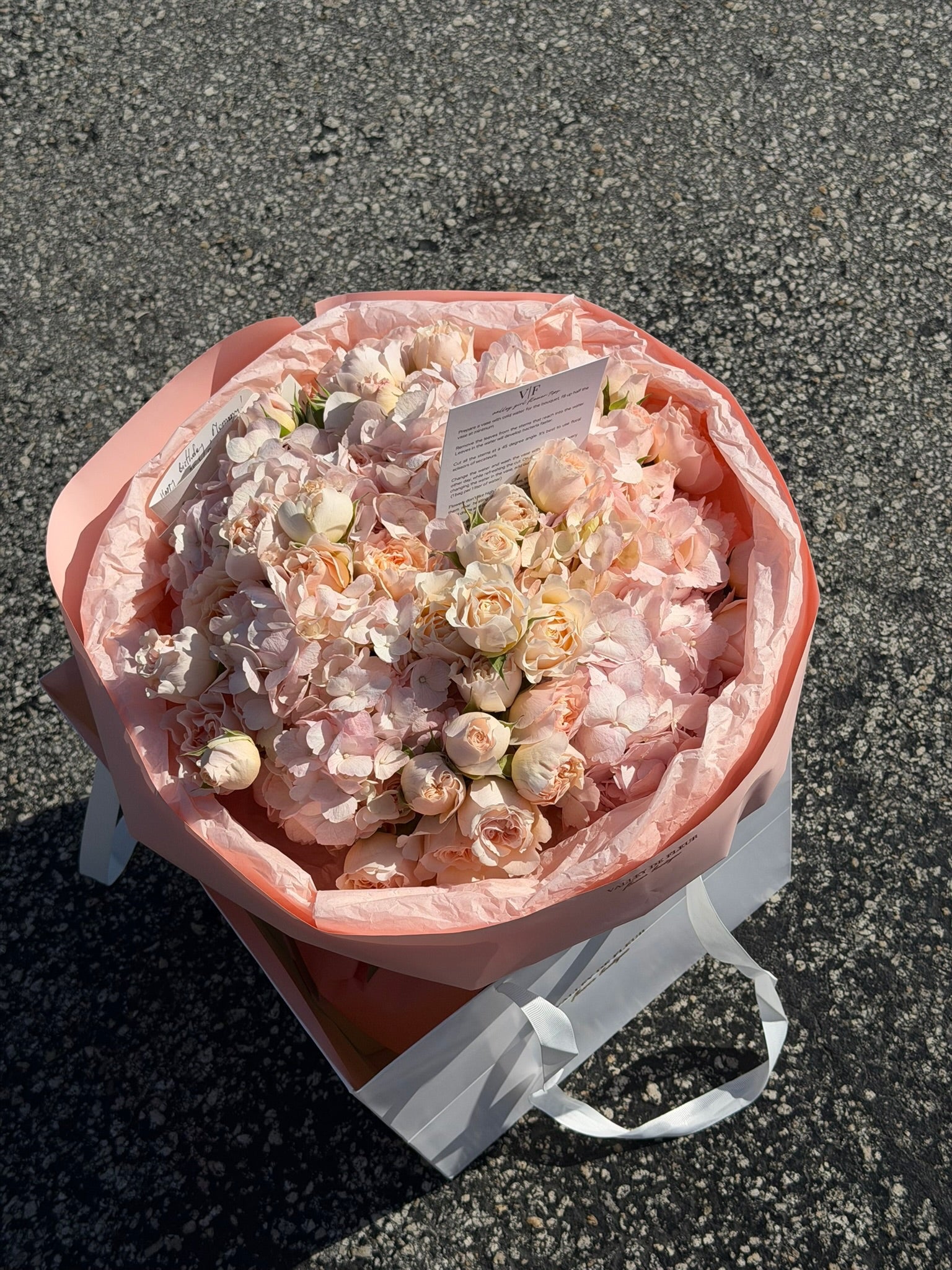 Light pink hydrangeas with clustered blush spray roses in a wrapped birthday arrangement